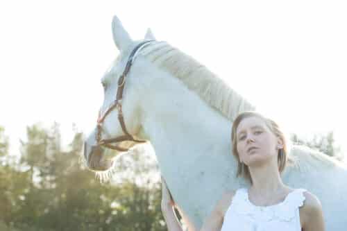 gegenlicht-portrait einer Frau mit weißem Pferd